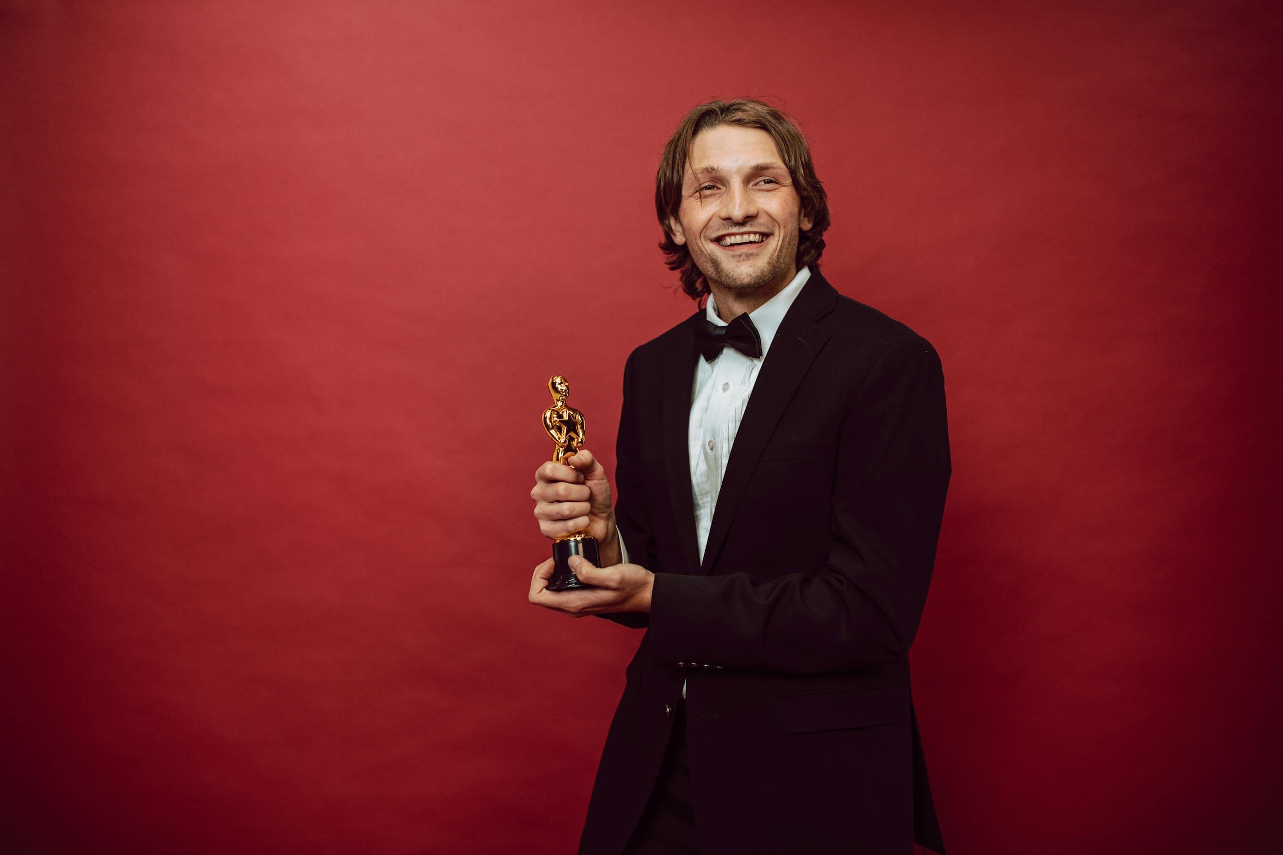 Portrait of a happy man in a suit holding a trophy on a red backdrop, celebrating success.